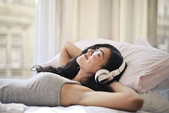 A woman with heads lying on a bed, enjoying music in a relaxed, cozy setting. HD wallpaper