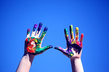 Colorful painted hands raised against a clear blue sky, symbolizing creativity and diversity. HD wallpaper