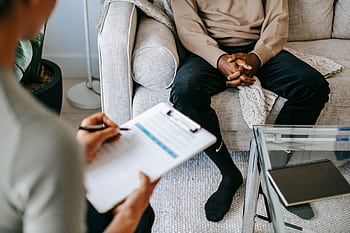 Therapist takes notes as client sits on a sofa during a psychotherapy session. HD wallpaper