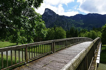 A scenic wooden bridge amidst vibrant greenery and towering mountain backdrop, perfect for travel and nature themes. HD wallpaper