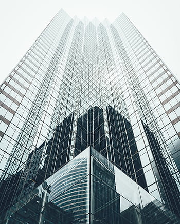 Striking low angle view of a modern skyscraper with reflective glass facade in a cityscape. HD phone wallpaper
