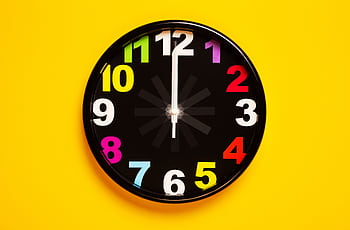 Vibrant wall clock with colorful numbers on a bright yellow background, emphasizing modern decor. HD wallpaper