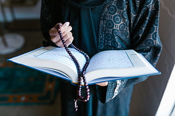 A woman in traditional attire reads a holy book with prayer beads, symbolizing faith and devotion. HD wallpaper