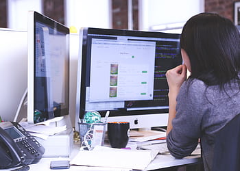 Professional woman focused on work using dual monitors in a modern office. HD wallpaper