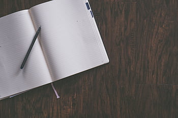 An open notebook with a pen resting on a wooden desk, ideal for productivity themes. HD wallpaper