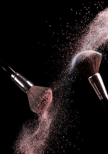 High-speed capture of makeup brushes dispersing pink powder in motion against a dark background. HD phone wallpaper