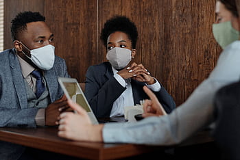 Diverse team discussing strategies while wearing face masks in a meeting room. HD wallpaper