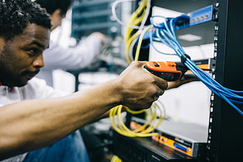 An engineer inspects network cables and connections in a server room, focusing with precision. HD wallpaper