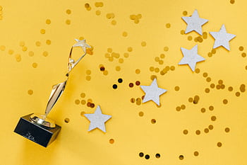 Shiny golden trophy and stars on a vibrant yellow background, symbolizing success and victory. HD wallpaper