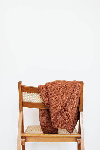 A cozy brown knit sweater draped over a wooden chair against a white background. Perfect fall fashion inspiration. HD phone wallpaper