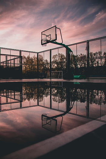 A tranquil view of a basketball court with reflections during sunset, creating a serene urban landscape. HD phone wallpaper