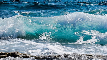 Dynamic ocean waves splashing against rocky shore, capturing sea foam and deep blue hues. HD wallpaper