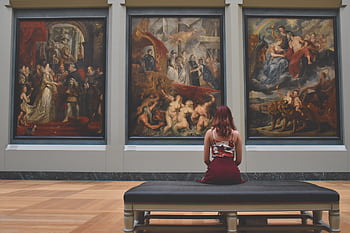 A woman observes classic paintings in an elegant museum gallery. HD wallpaper