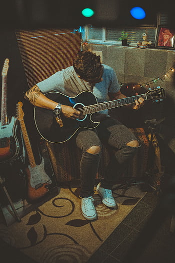A young man plays guitar in a cozy, dimly lit room, creating a musical atmosphere. HD phone wallpaper