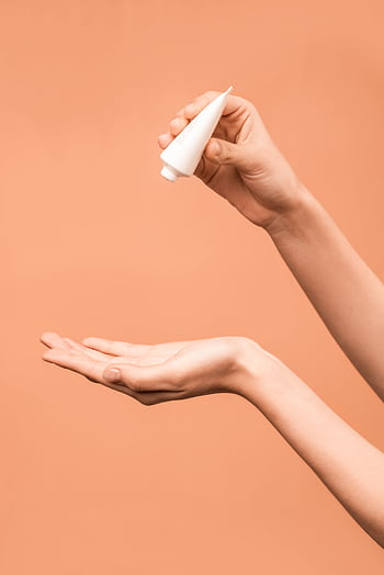 Close-up of hands applying lotion from a tube against a peach background. HD phone wallpaper