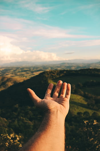 A hand reaching out towards a scenic view of mountains and sky, depicting dom and exploration. HD phone wallpaper
