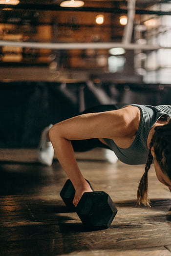 Fit woman doing a dumbbell push-up in a gym, highlighting strength and fitness training. HD phone wallpaper