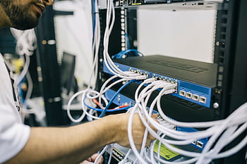 An IT professional configuring network cables in a server rack, focusing on Ethernet connections. HD wallpaper