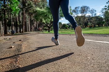 A woman running outdoors on a sunny day along a scenic park trail, focusing on fitness and health. HD wallpaper