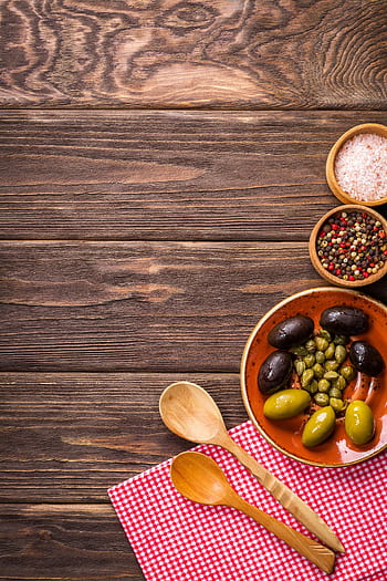 A rustic kitchen scene featuring olives and spices on a wooden table, creating a cozy culinary atmosphere. HD phone wallpaper