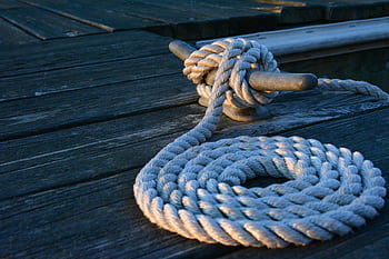 Close-up of a sturdy nautical knot on a weathered wooden dock at sunset. HD wallpaper