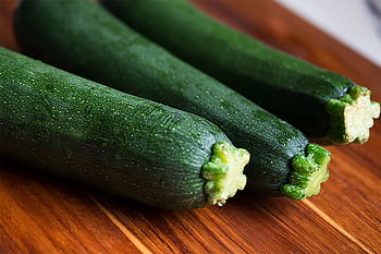 Close-up of three fresh green zucchinis on a wooden surface, perfect for food themes. HD wallpaper
