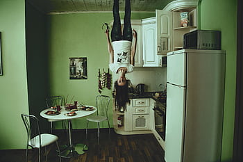 A person hangs upside down in a modern kitchen setting, creating a surreal ambiance. HD wallpaper