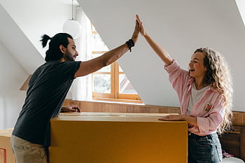 Young couple high-fiving in their new home, happily surrounded by moving boxes. HD wallpaper