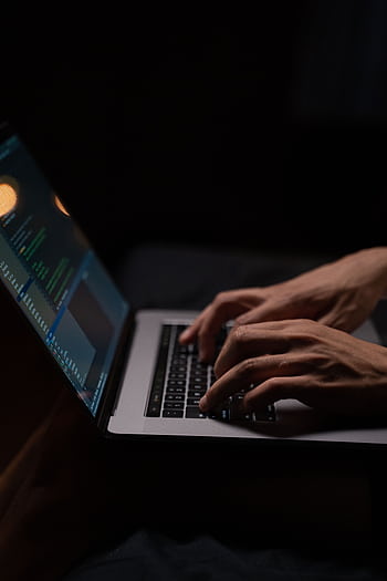 Hands typing code on a laptop keyboard in a dark room, capturing the essence of late-night programming. HD phone wallpaper