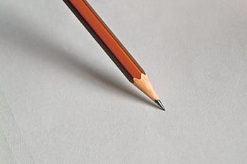 Detailed close-up of a wooden pencil resting on white paper, perfect for educational themes. HD wallpaper