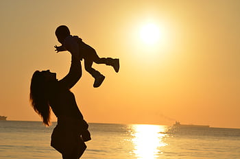 Silhouette of a mother lifting her child at a sunset beach, capturing warmth and love. HD wallpaper