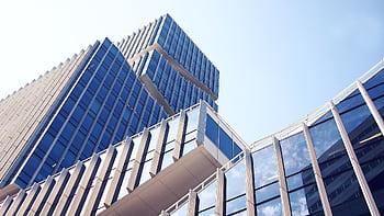 Low-angle shot of a modern skyscraper with reflective glass design under a clear blue sky. HD wallpaper