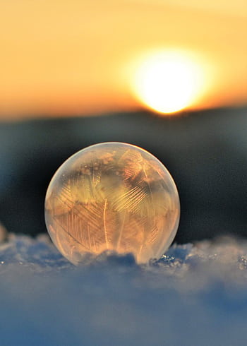 A frozen soap bubble on snow captures crystalline patterns against a sunrise backdrop. HD phone wallpaper
