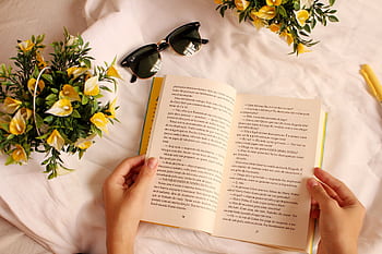 Hands holding a book surrounded by yellow flowers and sunglasses on a sunny day. HD wallpaper