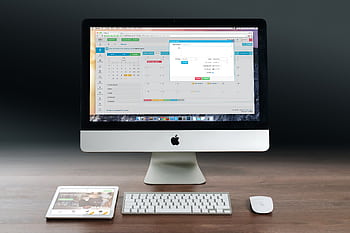A sleek office setup featuring an Apple iMac, iPad, and keyboard on a wooden desk. HD wallpaper