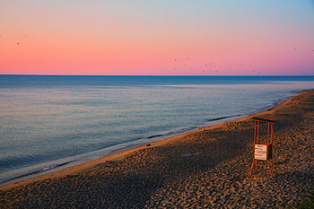 A tranquil beach scene featuring a lifeguard tower silhouetted against a colorful sunset sky over calm ocean waters. HD wallpaper