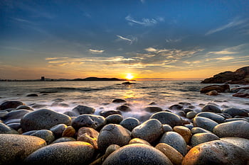Serene rocky shore landscape featuring a stunning sunset over the ocean with dramatic clouds. HD wallpaper