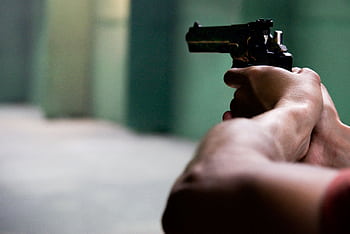 Close-up shot of hands aiming a pistol in an indoor shooting range, emphasizing focus and tension. HD wallpaper