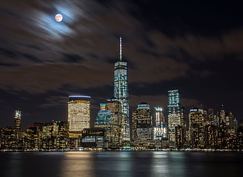 Captivating night view of New York City skyline under a full moon and reflective waters. HD wallpaper