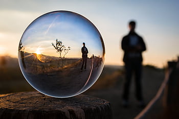 A stunning sunset captured through a glass sphere, showcasing a reflection of a standing silhouette. HD wallpaper