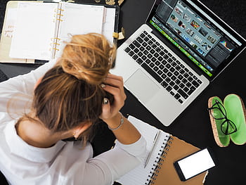 Overhead view of a stressed woman working at a desk with a laptop, , and notebooks. HD wallpaper