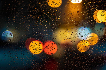Raindrops on window with vibrant bokeh lights creating an abstract nighttime view. HD wallpaper