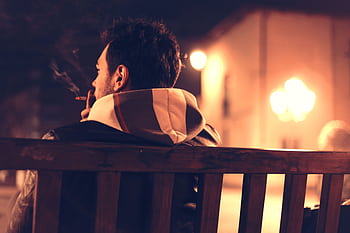 A man sits alone on a bench, smoking at night, creating a moody and atmospheric scene. HD wallpaper
