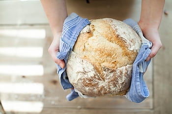Close-up of artisan bread held in hands with a blue cloth on a wooden table. HD wallpaper