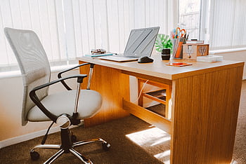 A modern office workspace featuring a wooden desk, chair, laptop, and bright natural light. HD wallpaper