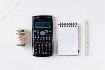 Top view of financial tools including a calculator, notepad, pen, and rolled cash on a white background. HD wallpaper