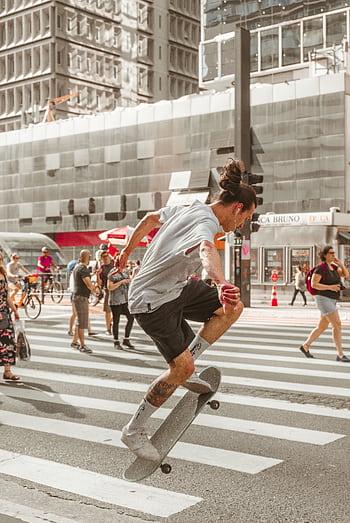 Skateboarder performing a trick on a busy city pedestrian crossing. HD phone wallpaper