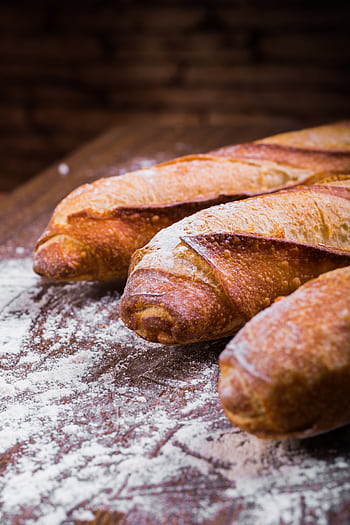 Close-up of fresh, golden-brown baguettes dusted with flour on a wooden table, showing texture and artisan quality. HD phone wallpaper