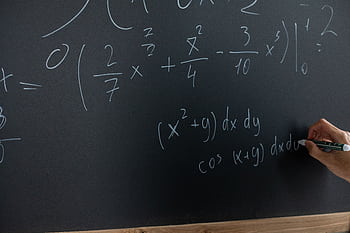 Hand writing mathematical equations on a chalkboard in a classroom setting. HD wallpaper