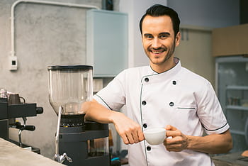 A cheerful barista in a coffee shop kitchen holding a coffee cup, ready to serve. HD wallpaper